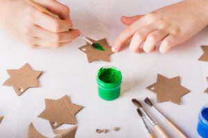 Children's hands paint a cardboard star for diy Christmas handmade decorations.